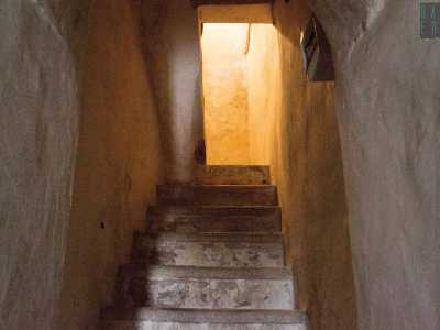 Per visitare il primo piano dobbiamo ora necessariamente spostarci sulla sinistra per accedere da una piccolissima porticina marrone. Saliamo a fatica una decina di gradoni alti e bianchi che ci conducono agli interni del palazzo